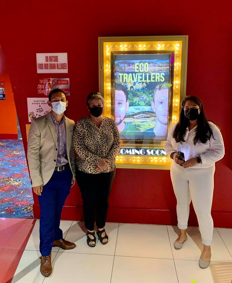Alex, Vicky, and Annette Arjoon standing next to a poster for EcoTravellers