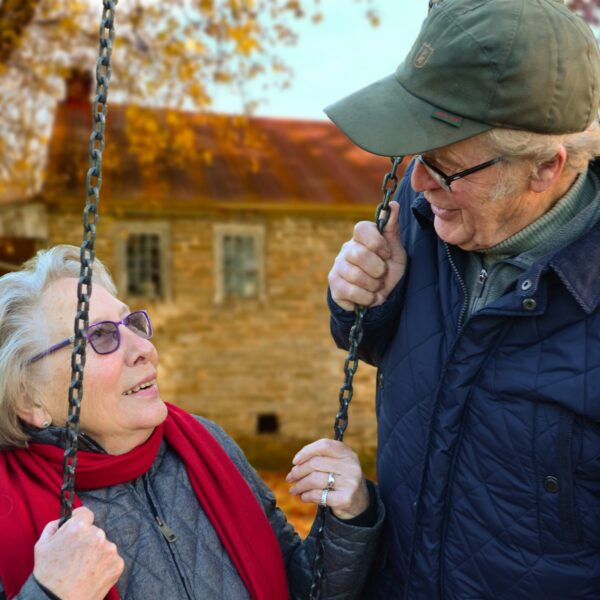 Elderly woman sitting on swing talking to an elderly man