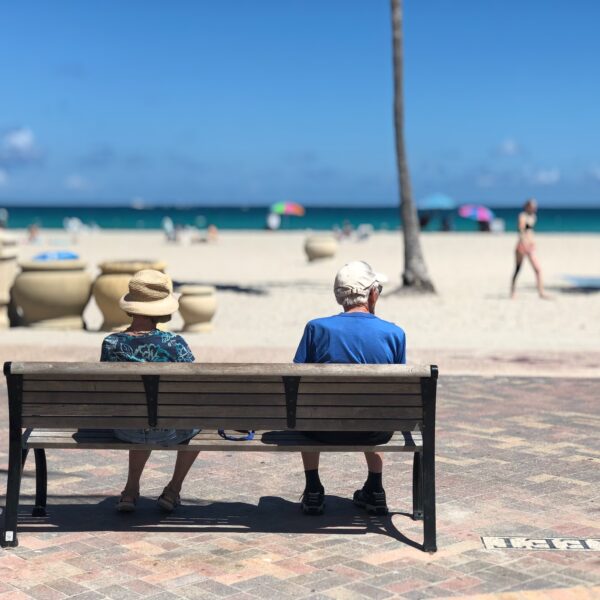 retired couple sitting on a bench looking at the beach