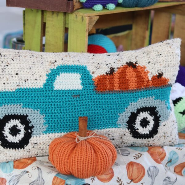A throw pillow with a pickup truck and pumpkins crocheted on it